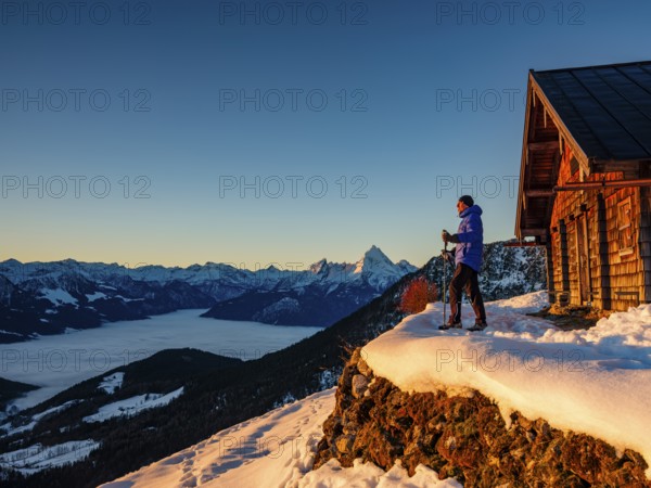 Mountaineers enjoy the sunrise in front of an alpine hut in winter, the Watzmann behind, fog in the valley, Berchtesgaden Alps, Scheibenkaser, Marktschellenberg, Berchtesgadener Land, Upper Bavaria, Bavaria, Germany