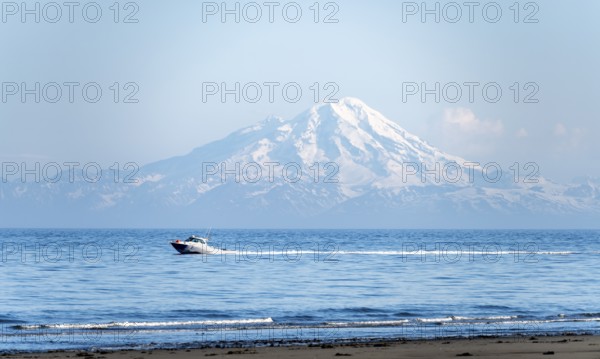 View over Cook Inlet to white mountain peaks of Mount Redoubt, motor boat rides on the ocean, Aleutian Mountains, Anchor Point, Anchor River State Recreation Area, Alaska, USA
