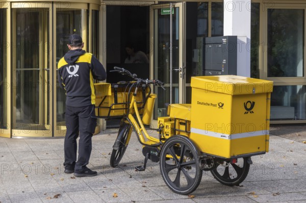 Deutsche Post mailmen on a bicycle through the city. Stuttgart, Baden-Württemberg, Germany