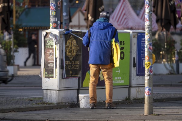 Man sticks posters to electrical boxes near Alexanderplatz, Berlin, Germany