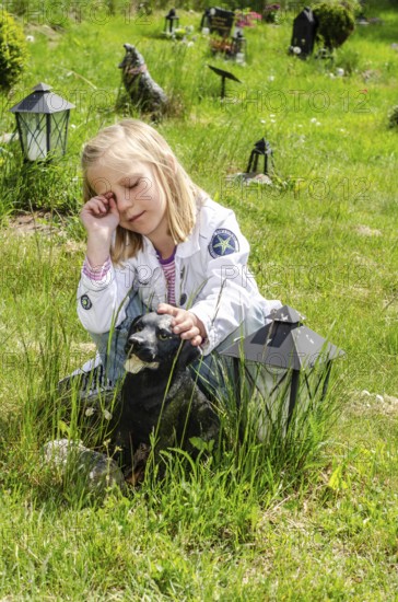 Grieving blonde 7-year-old girl at her dog's grave at pet cemetery in Ystad, Skåne County, Sweden, Scandinavia