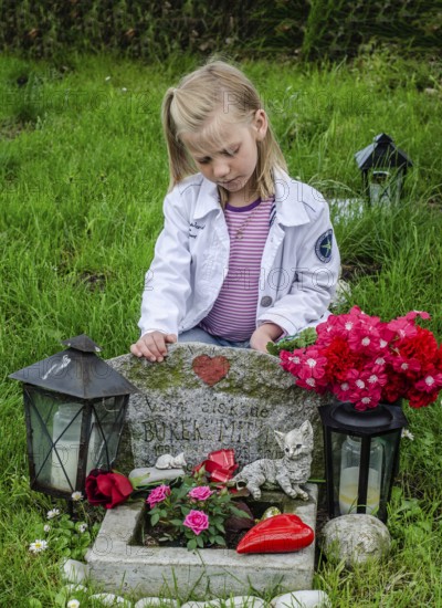 Grieving blonde 7-year-old girl at her cat's grave at pet cemetery in Ystad, Skåne County, Sweden, Scandinavia