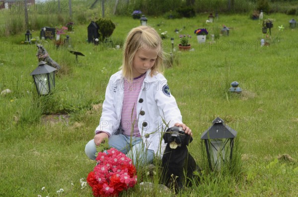 Grieving blonde 7-year-old girl at her dog's grave at pet cemetery in Ystad, Skåne County, Sweden, Scandinavia