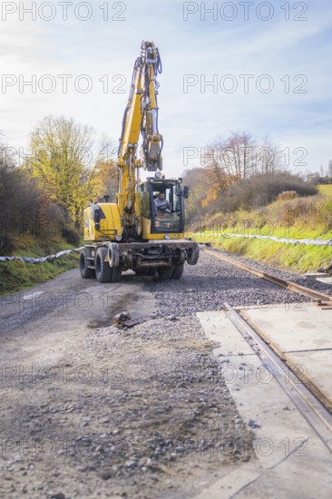 Yellow excavator lays tracks in autumn landscape, preparation of track work, track construction of the Hermann Hesse Railway, Calw, Germany