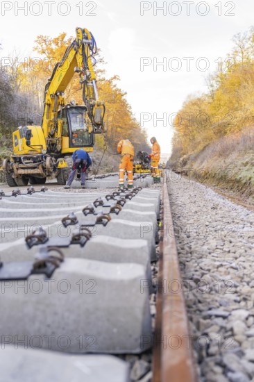 Workers lay concrete ties along an autumnal railway line with the help of an excavator, Hermann Hesse Railway track construction, Calw, Germany