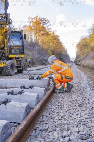 Workers lay concrete ties along a long railway line in an autumn landscape, track construction of the Hermann Hesse Railway, Calw, Germany