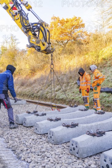 Construction workers supervise the use of an excavator for laying concrete ties, Hermann Hesse Railway track construction, Calw, Germany