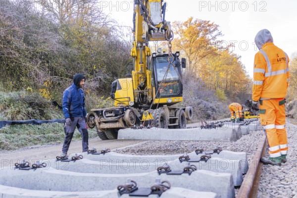 Track construction with a yellow excavator, where workers lay heavy concrete ties, Hermann Hesse Railway track construction, Calw, Germany