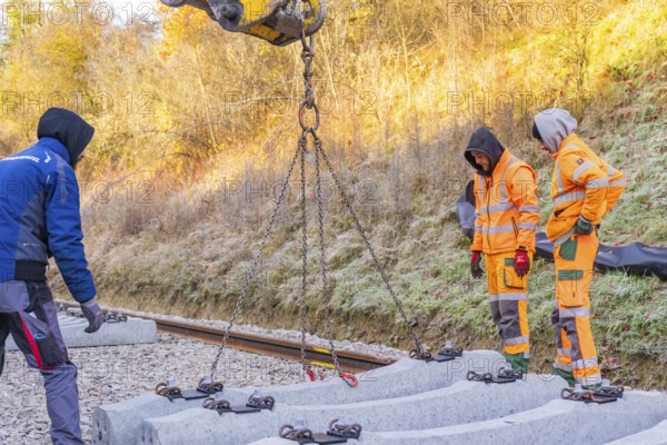 Workers lay concrete ties with an excavator under sunny autumn skies, Hermann Hesse Railway track construction, Calw, Germany