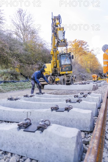 Workers use an excavator to lay concrete blocks along the tracks in autumn surroundings, track construction of the Hermann Hesse Railway, Calw, Germany