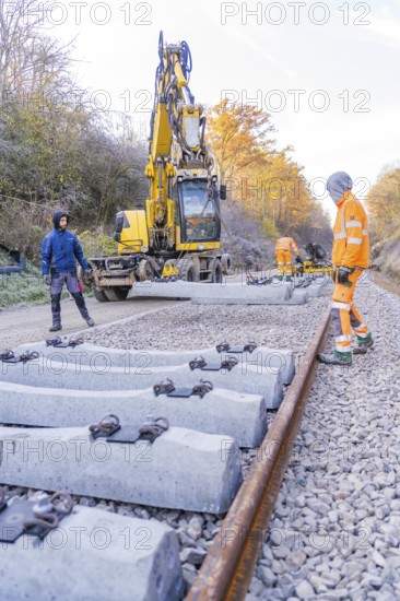 Construction workers lay concrete ties with a yellow excavator on a railway line in autumn, track construction of the Hermann Hesse Railway, Calw, Germany