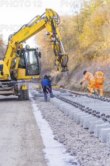 Excavators and workers lay rail blocks on a construction site on an autumn day, track construction by the Hermann Hesse Railway, Calw, Germany