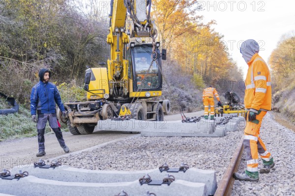 Workers lay concrete blocks for rails with an excavator on a construction site, track construction of the Hermann Hesse Railway, Calw, Germany
