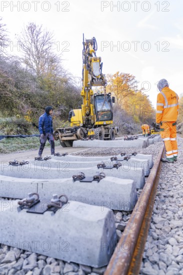 Concrete ties are laid with an excavator along a railway line, supervised by workers, track construction of the Hermann Hesse Railway, Calw, Germany