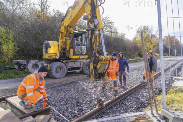 Construction workers in orange clothing work next to a yellow excavator on a railway line, track construction of the Hermann Hesse Railway, Calw, Germany