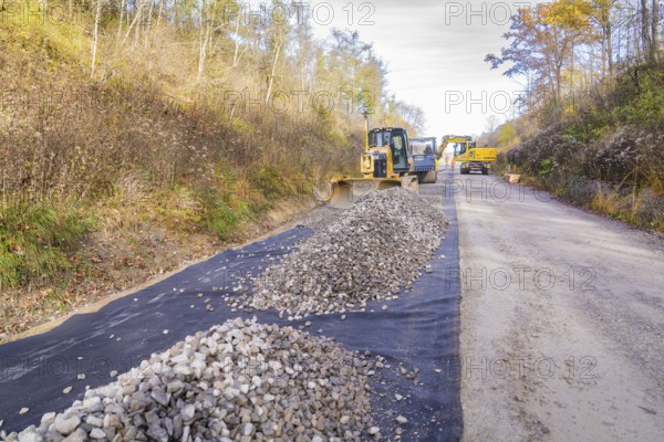 Several construction machines move gravel on a country road in autumn, track construction by the Hermann Hesse Railway, Calw, Germany