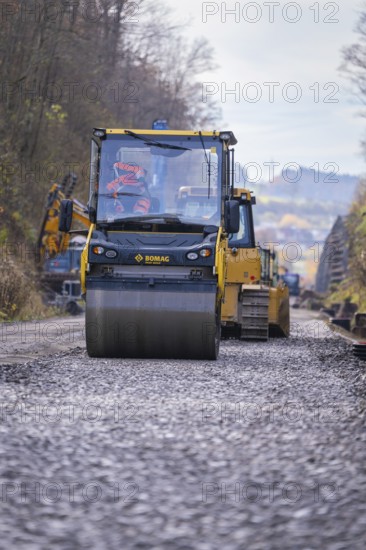 Bomag road roller rolls over gravel for compaction during road work, Hermann Hesse Railway track construction, Calw, Germany