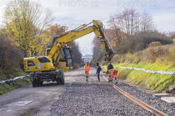 Yellow excavator on a construction site in autumn, workers laying tracks on gravel, Hermann Hesse Railway track construction, Calw, Germany