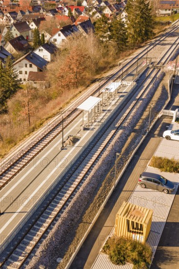 Aerial view of a small train station with parked cars surrounded by autumn vegetation and a village, new Hermann Hessebahn railway station, Ostelsheim, Calw district, Germany