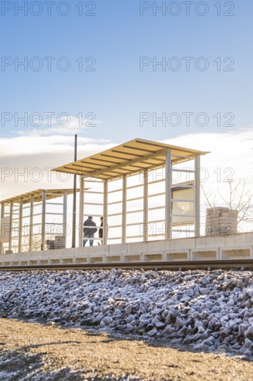 Two people at a modern bus stop under blue sky, new Hermann Hessebahn railway station, Ostelsheim, Calw district, Germany