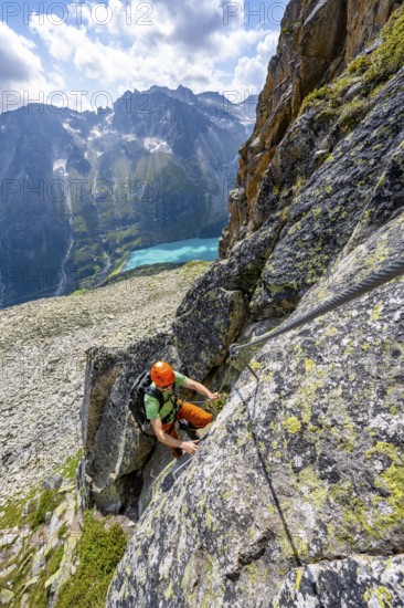 Mountaineer climbs on steep rock face in the secured via ferrata Crocodile Mountain Lake at Bergseeschijen-Vorbau, Göscheneralp, Canton of Uri, Switzerland