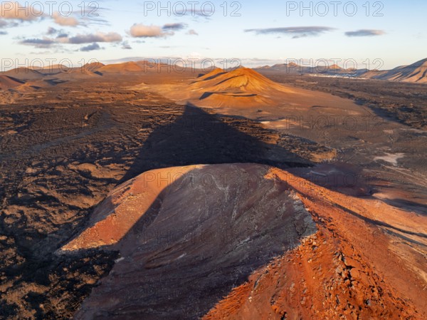 Picturesque volcanic landscape in evening light, red volcano Montaña Bermeja between lava fields, aerial view, Lanzarote, Canary Islands, Spain