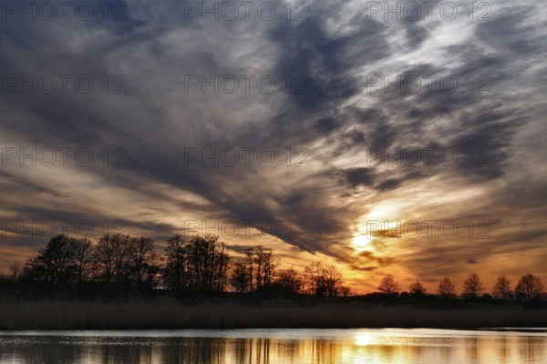 Dramatic sunset sky with trees and soft reflection in water, Peenetal nature park Park, Mecklenburg-Western Pomerania, Germany