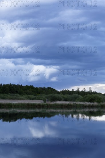 Cloudy sky over a quiet river with trees in the background, Peenetal nature park Park, Mecklenburg-Western Pomerania, Germany