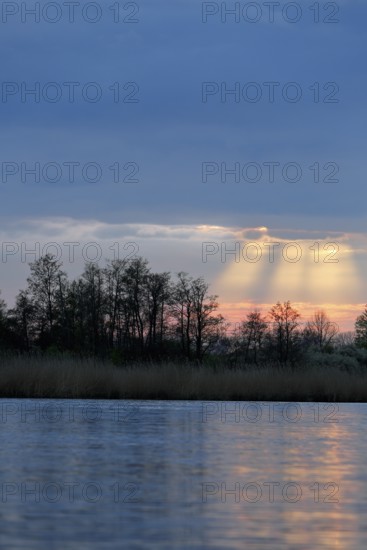 Sunbeams through clouds over a river at dusk, Peenetal nature park Park, Mecklenburg-Western Pomerania, Germany
