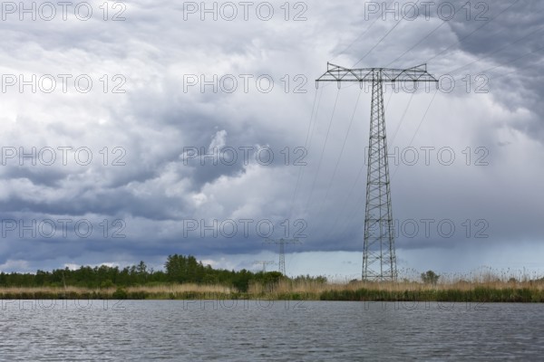 Landscape with high power pole under dramatic waterside cloud formations, Peenetal nature park Park, Mecklenburg-Western Pomerania, Germany
