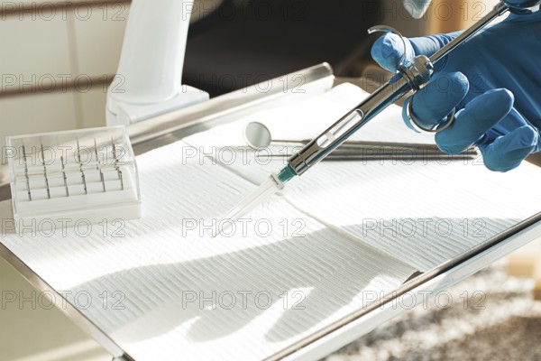 The dentist's hand, in a blue glove, holds a carpal syringe on a tray, ready for a medical procedure