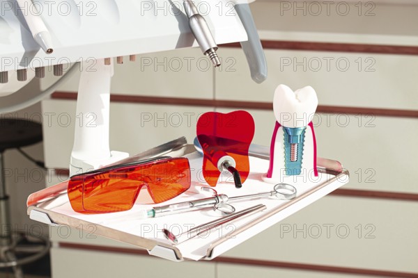 On the tray are various dental instruments, a model dental implant and bright orange safety glasses, ready for use in clinical dental settings