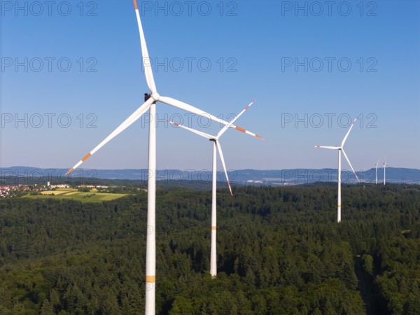 Three wind turbines rise above a green forest under a clear sky, near Schorndorf, Remstal, Baden-Württemberg, Germany