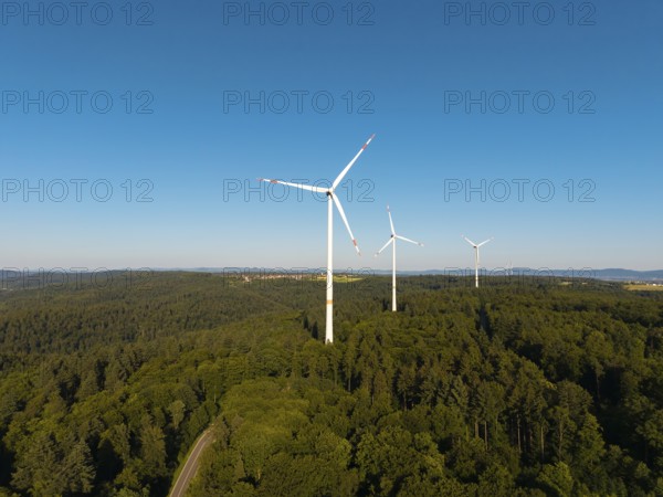 A series of wind turbines on a wooded hill under a wide blue sky, near Schorndorf, Remstal, Baden-Württemberg, Germany