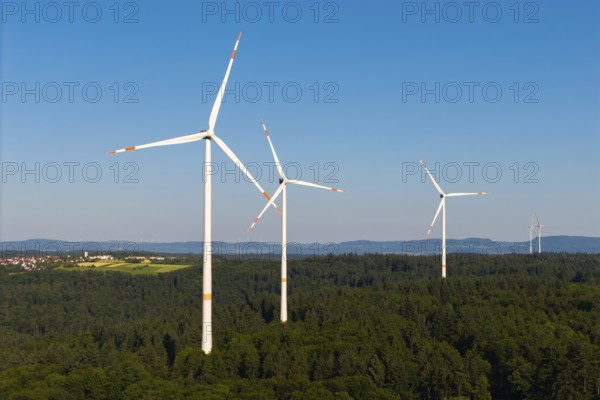 Wind turbines stand in a wooded landscape under a wide blue sky, near Schorndorf, Remstal, Baden-Württemberg, Germany