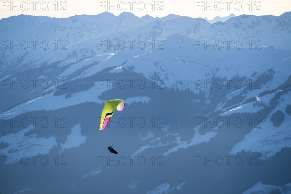 Paragliders flying over snowy mountain peaks in winter in evening light, Kitzbühel Alps, Tyrol, Austria