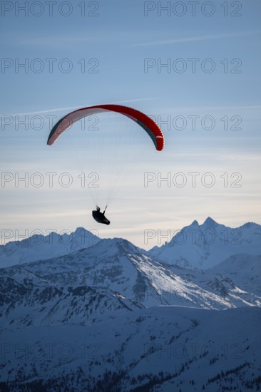 Paragliders flying over snowy mountain peaks in winter in evening light, Kitzbühel Alps, Tyrol, Austria