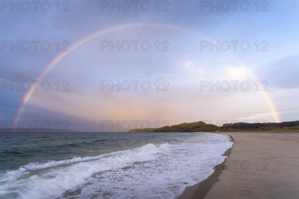Landscape with sea and sandy beach in New Zealand with rainbow, in the evening at golden hour. Otama Beach, Coromandel Peninsula, Waikato, New Zealand