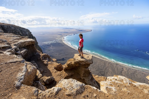 Woman enjoying the view from the Risco de Famara cliffs on Famara beach, Playa de Famara with La Calaeta, Lanzarote, Canary Islands, Spain