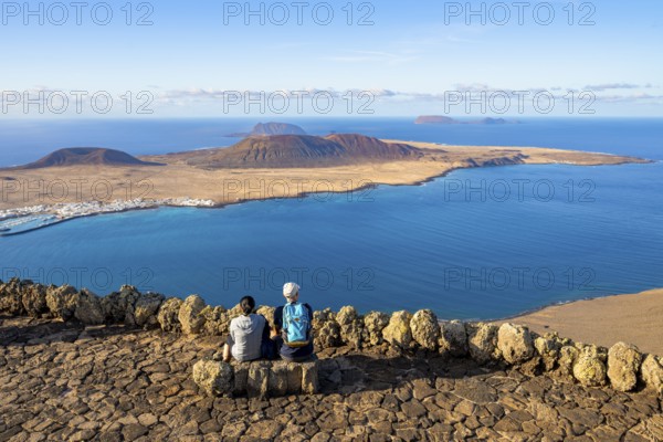 Tourists on a bench on the viewing platform at the Mirador del Río viewpoint, in the evening light, view of the sea and of the island of La Graciosa with volcanic craters, designed by artist César Manrique, Lanzarote, Canary Islands, Spain