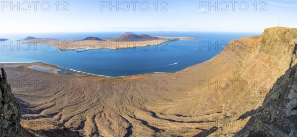 View of steep cliffs by the sea and island of La Graciosa with volcanic craters in the evening light, Mirador del Río viewpoint designed by artist César Manrique, Lanzarote, Canary Islands, Spain