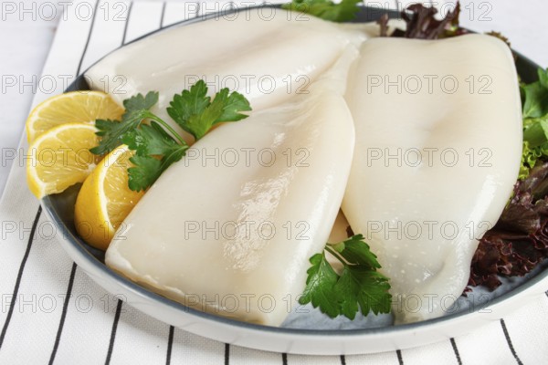 Fresh squid on a black plate with greens and lemon slices prepared for cooking in a kitchen setting
