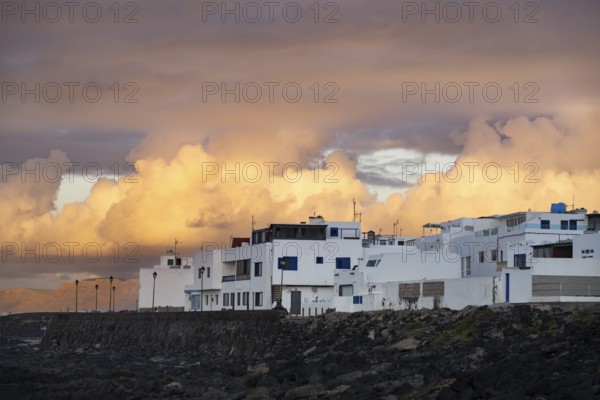 Black coast of volcanic rocks behind typical white houses of the village of La Santa, at sunset, Lanzarote, Canary Islands, Spain