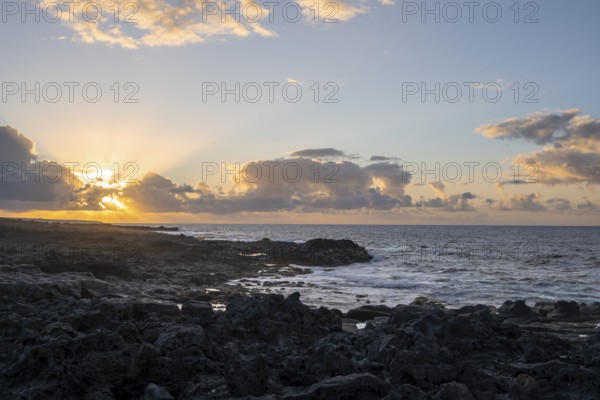 Dramatic cloudy sky with sunbeams at sunset, seaside coast with volcanic rocks, La Santa, Lanzarote, Canary Islands, Spain