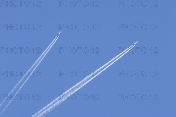 Two jet passenger aircraft flying in a blue sky with contrails or vapour trails behind, England, United Kingdom