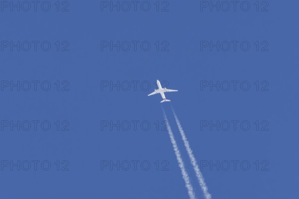 Jet passenger aircraft flying in a blue sky with contrails or vapour trails behind, England, United Kingdom