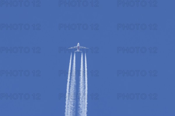 Airbus A380 jet passenger aircraft of Emirates airlines flying in a blue sky with contrails or vapour trails behind, England, United Kingdom