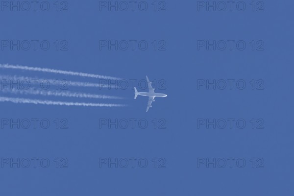 Jet commercial passenger aircraft flying in a blue sky with contrails or vapour trails behind, England, United Kingdom