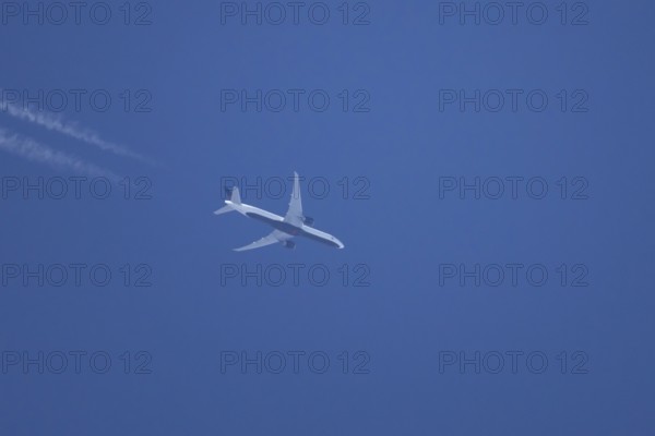 Boeing jet passenger aircraft flying in a blue sky with contrails or vapour trails behind, England, United Kingdom