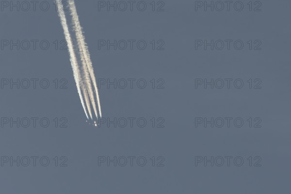 Jet passenger aircraft flying in a blue sky with contrails or vapour trails behind, England, United Kingdom